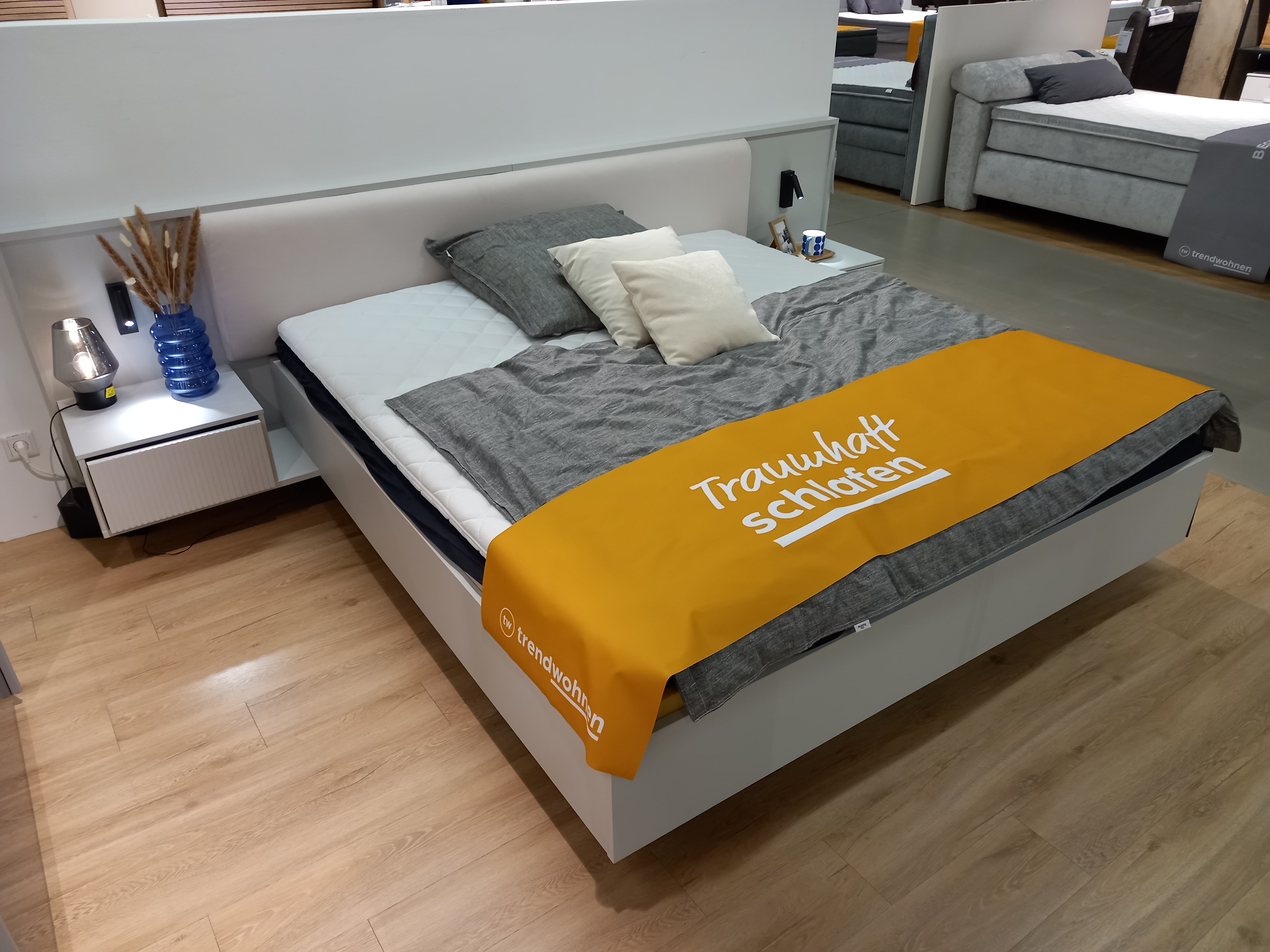 Bettanlage  in Farbe , Doppelbett, gepolstertes Kopfteil, graue Bettwäsche, weißer Bettrahmen, Nachttisch